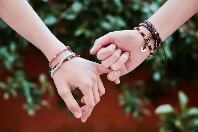 Two hands holding each other, symbolizing friendship and connection, adorned with colorful bracelets.