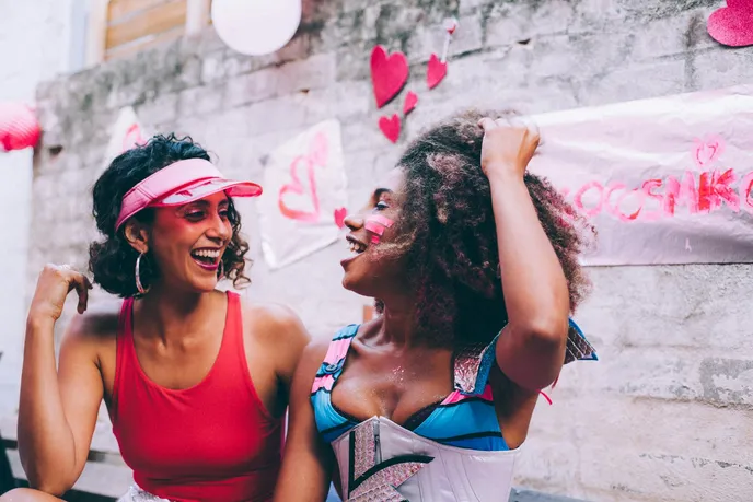 Two women laughing and having fun at a celebration, surrounded by decorative hearts and festive decor, embodying the joy and connection associated with love.