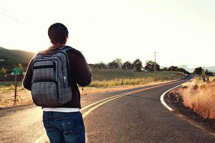 A person with a backpack walking along an empty, winding road during sunset, symbolizing the journey of life.