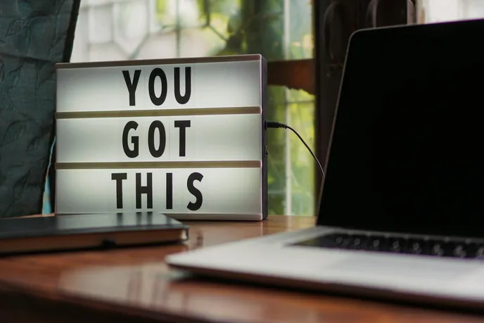 A motivational light box displaying the words 'YOU GOT THIS' next to a laptop and notebook, symbolizing encouragement and support in personal or professional pursuits.